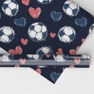 K&ouml;nnte beinhalten: Blaues Geschenkpapier mit einem sich wiederholenden Muster aus wei&szlig;en Fu&szlig;b&auml;llen und roten Herzen. Die Fu&szlig;b&auml;lle sind in einem einfachen, kritzelartigen Stil gezeichnet.