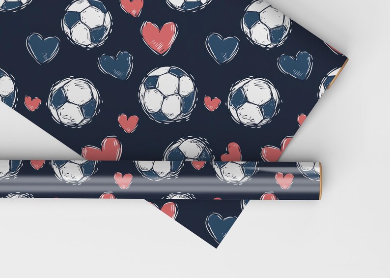 K&ouml;nnte beinhalten: Blaues Geschenkpapier mit einem sich wiederholenden Muster aus wei&szlig;en Fu&szlig;b&auml;llen und roten Herzen. Die Fu&szlig;b&auml;lle sind in einem einfachen, kritzelartigen Stil gezeichnet.