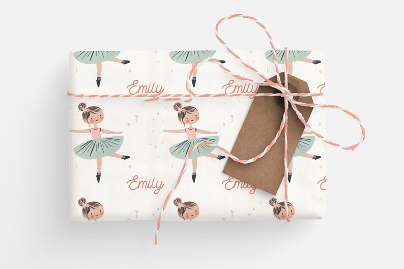 May include: White wrapping paper with a repeating pattern of a ballerina in a pink leotard and green tutu. The ballerina is holding her arms out to the side. The name "Emily" is written in pink cursive on the paper.