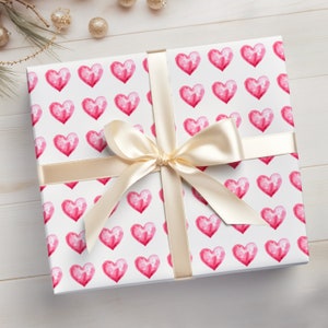 May include: A white gift box with a pink watercolor heart pattern. The box is tied with a cream-colored satin ribbon.