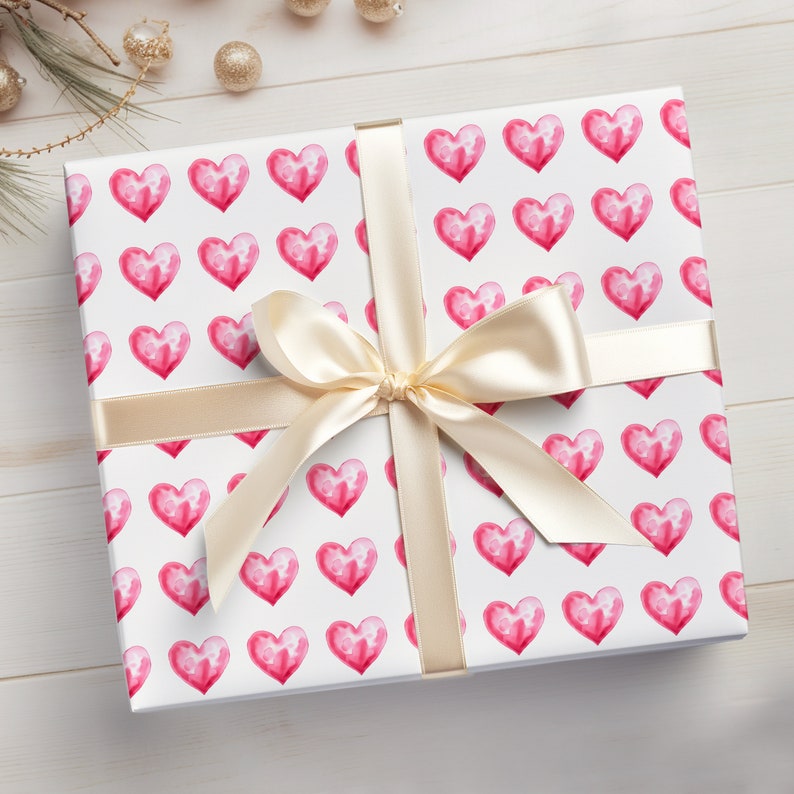 May include: A white gift box with a pink watercolor heart pattern. The box is tied with a cream-colored satin ribbon.