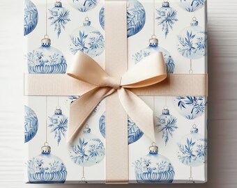 May include: A white gift box with a beige ribbon and bow. The box is wrapped in blue and white patterned paper with a design of hanging ornaments.
