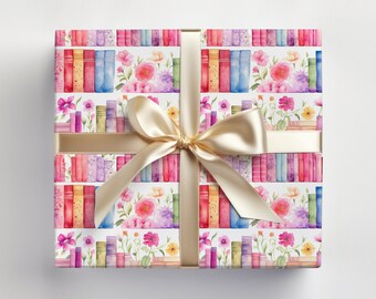 May include: A wrapped gift with a white background. The wrapping paper features a watercolor design of colorful books and flowers. A gold ribbon and bow adorn the package, creating a festive presentation.