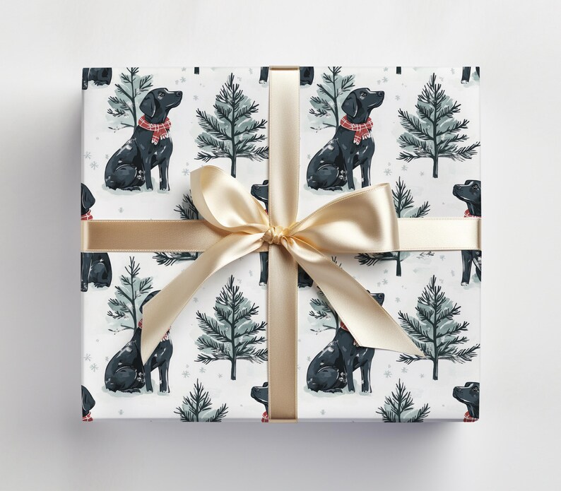 K&ouml;nnte beinhalten: Verpacktes Geschenk mit wei&szlig;em Hintergrund, das ein sich wiederholendes Muster aus schwarzen Labrador-Retrievern mit roten Schals und gr&uuml;nen Weihnachtsb&auml;umen zeigt. Ein goldenes Band und eine Schleife sind um das Geschenk gebunden.