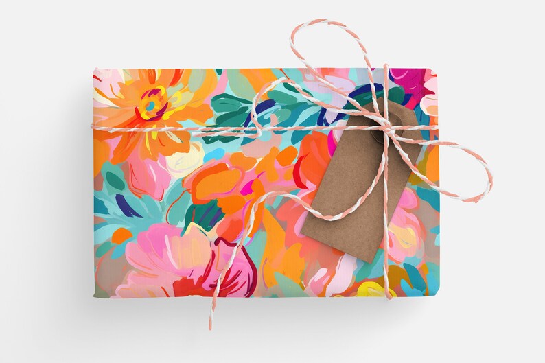 May include: A gift box wrapped in colourful floral patterned paper with a brown paper tag tied with a pink and white twine bow.