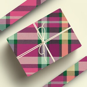 May include: A pink, green, and cream plaid gift box wrapped with twine. The box is sitting on a white surface.