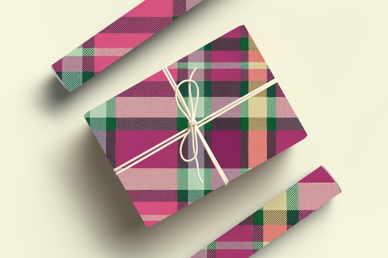May include: A pink, green, and cream plaid gift box wrapped with twine. The box is sitting on a white surface.