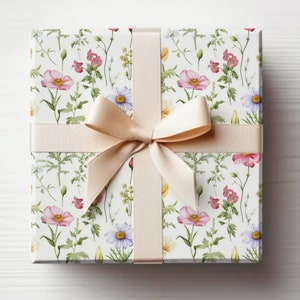 May include: A white gift box with a floral pattern featuring pink, yellow, and blue flowers. The box is tied with a cream-colored satin ribbon with a bow.