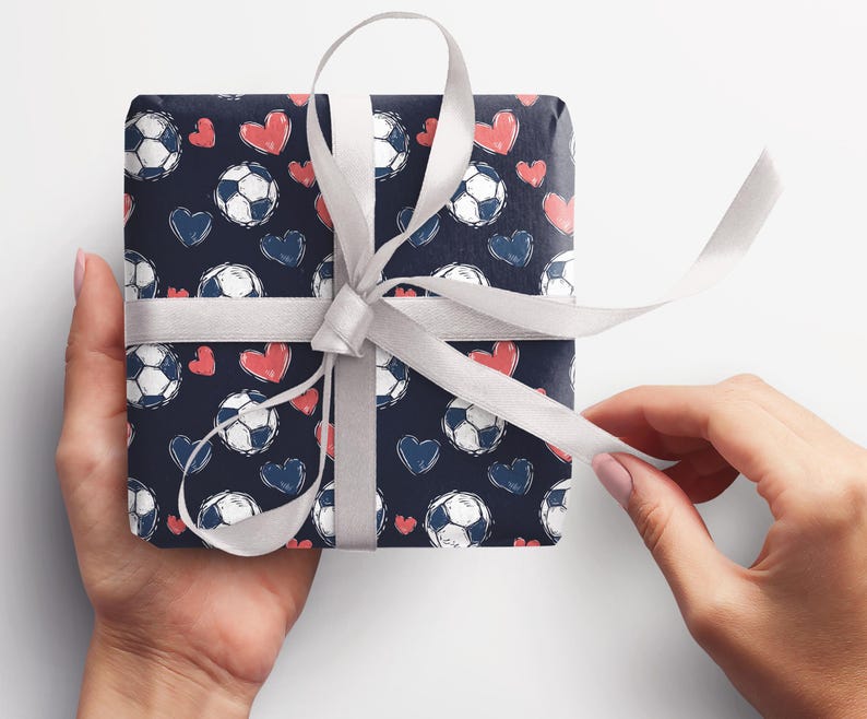 K&ouml;nnte beinhalten: Ein Geschenk, das in blaues Geschenkpapier mit einem wei&szlig;en Band eingewickelt ist. Das Papier hat ein Muster aus wei&szlig;en Fu&szlig;b&auml;llen und rosa Herzen.