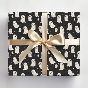 May include: Black and white wrapping paper with a repeating pattern of white ghosts on a black background. The paper is tied with a gold ribbon.