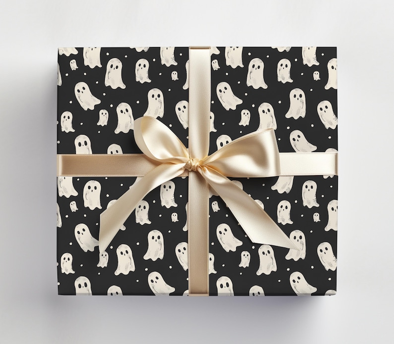 May include: Black and white wrapping paper with a repeating pattern of white ghosts on a black background. The paper is tied with a gold ribbon.