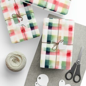 May include: Three wrapped gifts with a watercolor plaid pattern in shades of red, green, and white. The gifts are tied with twine and decorated with white paper stars and hearts.