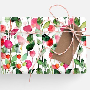 May include: A white gift wrap with a watercolor floral pattern featuring pink and red flowers, green leaves, and white stems. The gift wrap is tied with a pink and white twine and a brown gift tag.