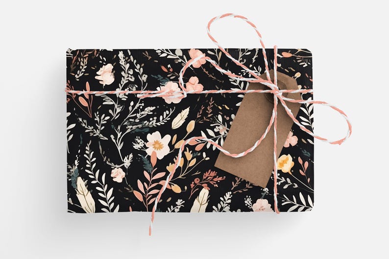 Op de afbeelding: Een zwarte cadeaudoos met een bloemenpatroon in roze, wit en gele tinten. De doos is vastgebonden met een wit en roze touwtje en heeft een bruin papieren label.