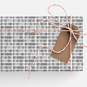 May include: Gift-wrapped present with a binary code pattern in black and white. The package is tied with a pink and white twine and a brown tag. The gift is ready to be given.