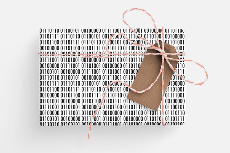 May include: Gift-wrapped present with a binary code pattern in black and white. The package is tied with a pink and white twine and a brown tag. The gift is ready to be given.