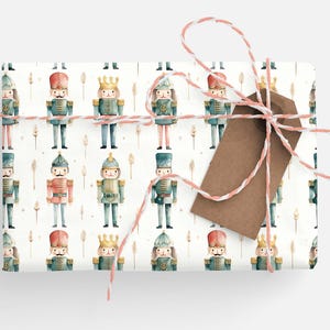 May include: White wrapping paper with a repeating pattern of watercolor nutcracker soldiers. The nutcrackers are wearing blue and red uniforms with gold accents. The paper is tied with a brown and white twine bow.