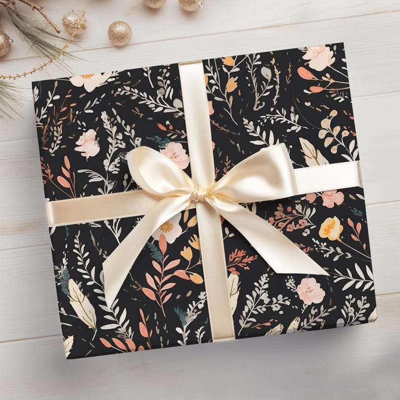 Op de afbeelding: Een zwarte cadeaudoos met een bloemenpatroon in roze, oranje en gele tinten. De doos is gebonden met een cr&egrave;mekleurig satijnen lint.