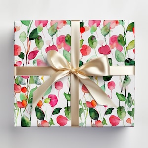 May include: A white gift wrap with a watercolor pattern of pink and green flowers and leaves. The gift wrap is tied with a gold ribbon.