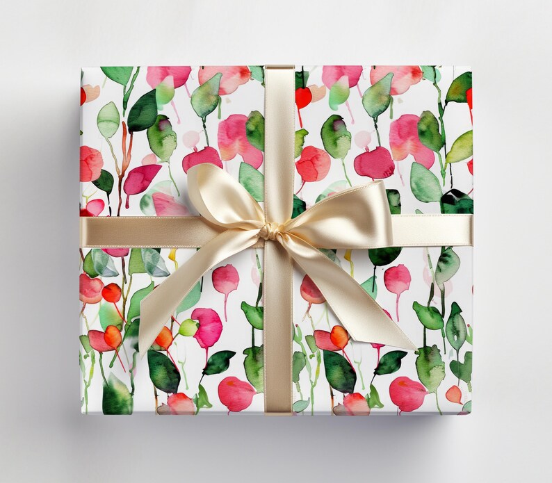 May include: A white gift wrap with a watercolor pattern of pink and green flowers and leaves. The gift wrap is tied with a gold ribbon.