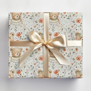 May include: A white gift wrap with a repeating pattern of brown bears wearing sweaters and orange flowers. The gift wrap is tied with a gold ribbon.