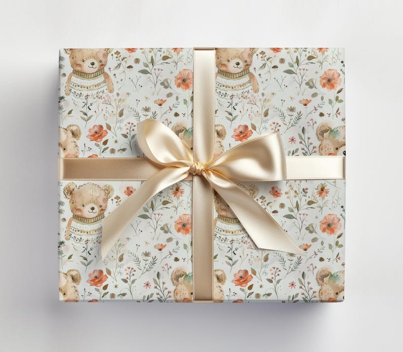 May include: A white gift wrap with a repeating pattern of brown bears wearing sweaters and orange flowers. The gift wrap is tied with a gold ribbon.