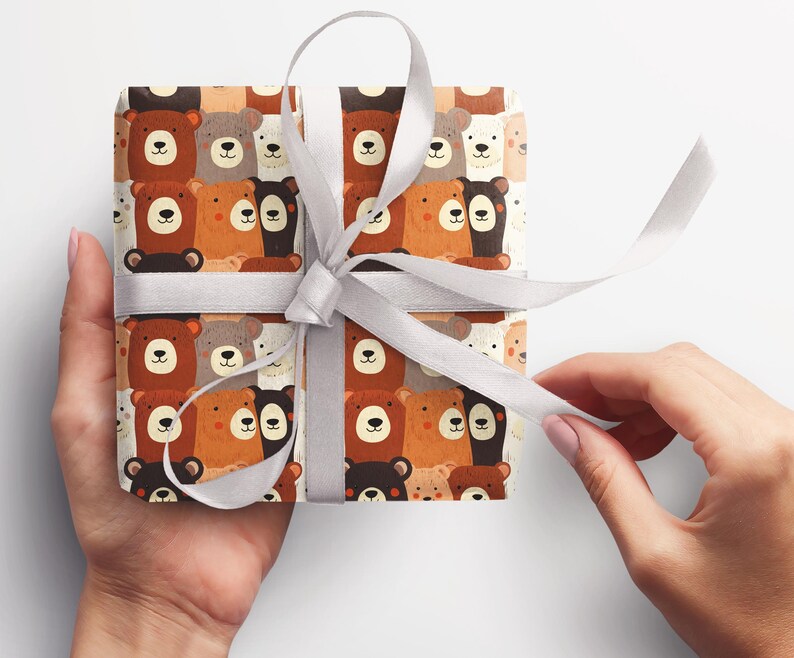 Op de afbeelding: Wit cadeaupapier met een herhalend patroon van bruine, zwarte en witte beren. De beren kijken allemaal naar voren en hebben verschillende gezichtsuitdrukkingen. Het cadeaupapier is vastgebonden met een wit lint.