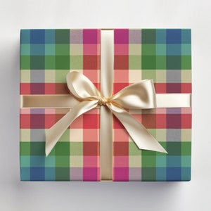 May include: A square gift box wrapped in colorful plaid paper. The plaid pattern features a mix of blue, green, red, and pink squares. A cream-colored satin ribbon is tied in a bow on top, adding a touch of elegance to the present.