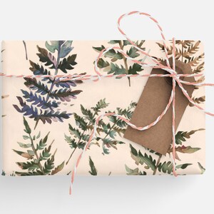 May include: A gift wrapped in cream paper with a watercolor fern pattern. The gift is tied with a pink and white twine and a brown gift tag.