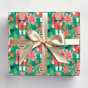 May include: Green wrapping paper with a repeating pattern of nutcracker soldiers and pink flowers. A gold ribbon is tied around the paper.