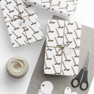 K&ouml;nnte beinhalten: Wei&szlig;es Geschenkpapier mit einem sich wiederholenden Muster aus Hockeyschl&auml;gern, die mit bunten Weihnachtslichtern verziert sind. Das Papier ist um eine Geschenkbox mit einer braunen Schnur gebunden.