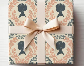 Peut inclure: Un coffret cadeau emballé avec un ruban et un nœud crème. Le papier d'emballage présente un motif répété d'une silhouette de femme dans une couronne de feuilles roses et bleues sur fond crème.