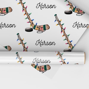 K&ouml;nnte beinhalten: Wei&szlig;es Geschenkpapier mit einem sich wiederholenden Muster aus Hockeyschl&auml;gern mit Weihnachtslichtern und dem Namen "Karson".