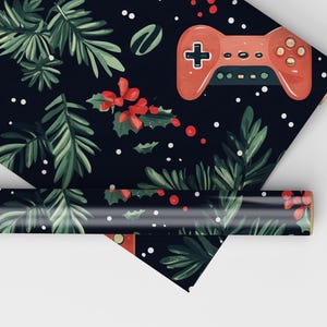 K&ouml;nnte beinhalten: Geschenkpapier mit dunkelblauem Hintergrund, verziert mit gr&uuml;nen Tannenzweigen, roten Beeren und einem roten Videospiel-Controller. Wei&szlig;e Punkte vervollst&auml;ndigen das festliche Urlaubsdesign.