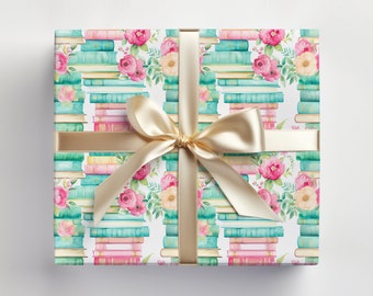 May include: A white gift wrap with a pattern of stacked books and pink flowers. A gold ribbon is tied around the box with a bow.