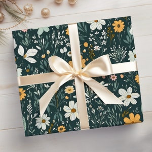May include: A gift box wrapped in dark green wrapping paper with a floral pattern featuring white, yellow, and pink flowers. A cream-colored satin ribbon is tied in a bow on top of the box.