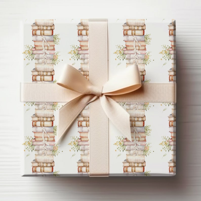May include: A white gift box with a beige ribbon and bow. The box is wrapped in paper with a repeating pattern of stacks of books and floral accents.