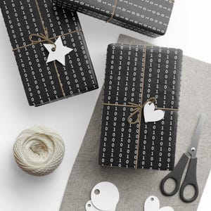 May include: Three black and white gift boxes wrapped in paper with a repeating pattern of 0s and 1s. The boxes are tied with twine and decorated with white paper stars and hearts.