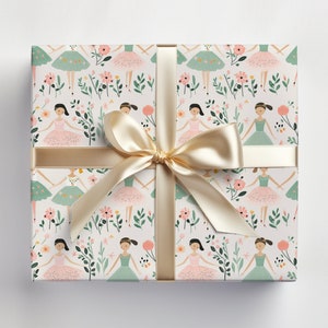 May include: A white gift wrap with a repeating pattern of pink and green ballerina figures with flowers and leaves. The gift wrap is tied with a gold ribbon.