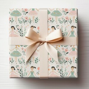 May include: A gift box wrapped in white paper with a pink and green ballerina pattern. The box is tied with a cream-colored satin ribbon.