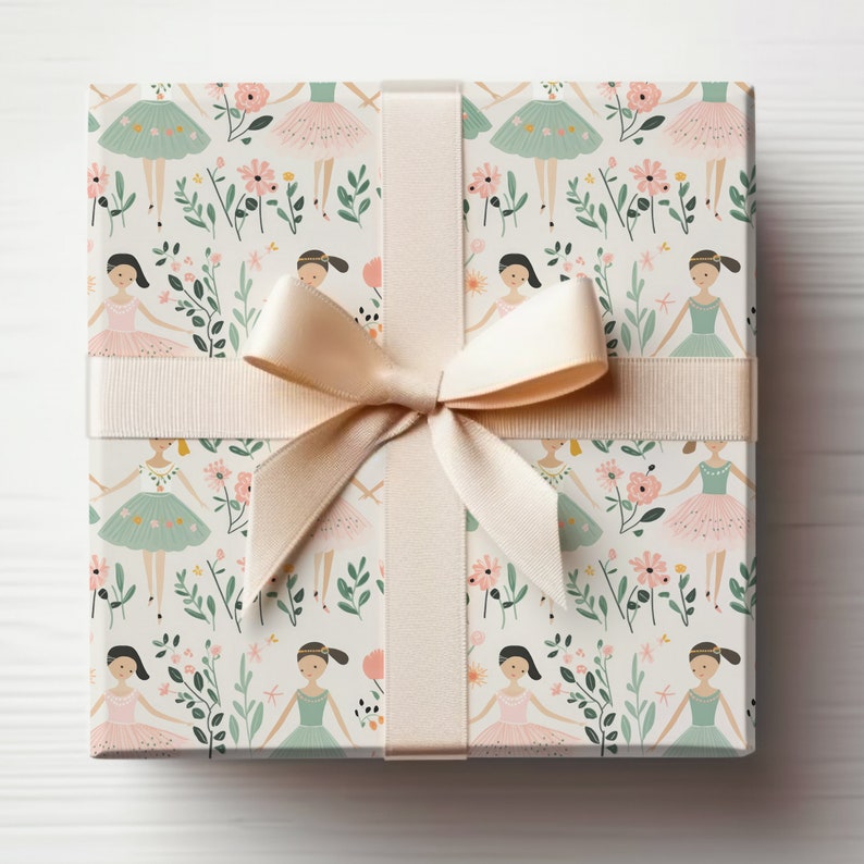May include: A gift box wrapped in white paper with a pink and green ballerina pattern. The box is tied with a cream-colored satin ribbon.