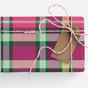 May include: A pink, green, and white plaid gift box tied with a white and peach twine bow and a brown gift tag.