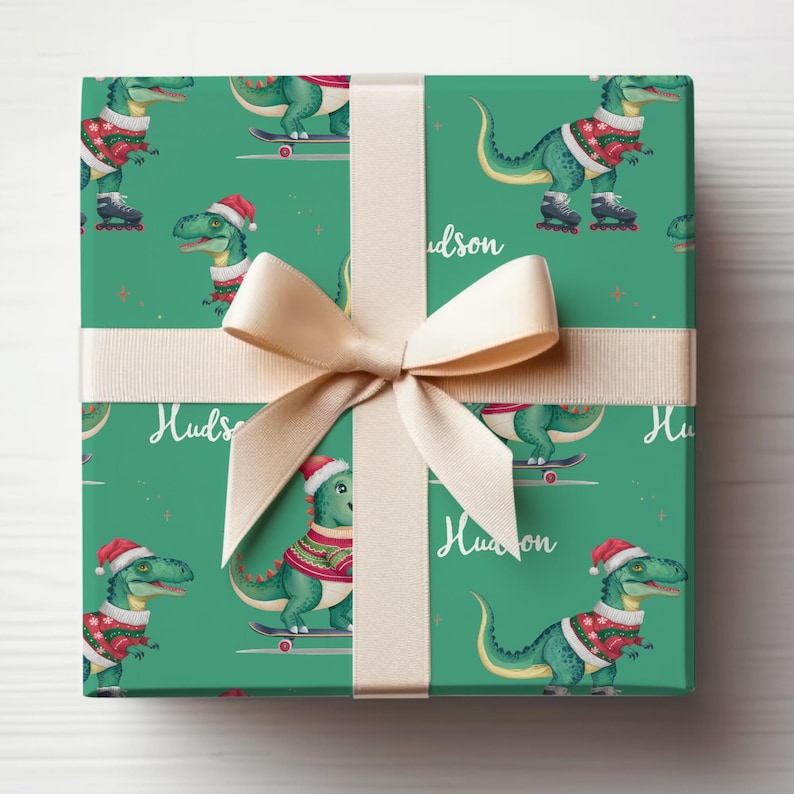 May include: Green wrapping paper with a repeating pattern of cartoon dinosaurs wearing Santa hats and riding skateboards. The paper is tied with a cream-coloured ribbon and the name "Hudson" is printed on the paper.