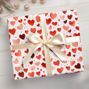Op de afbeelding: Een witte cadeaudoos met een rood en roze aquarelhartpatroon. De doos is gebonden met een cr&egrave;mekleurig satijnen lint.