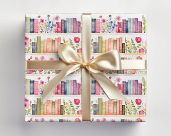 May include: White gift wrap with a repeating pattern of colorful books on a bookshelf with flowers. A gold ribbon is tied around the gift box.