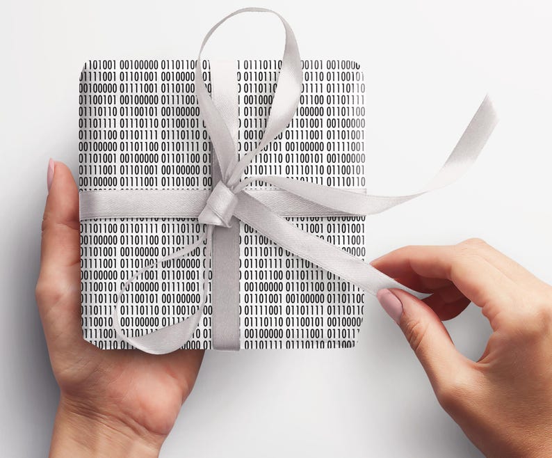 May include: A present wrapped in paper printed with a black and white binary code design, secured with a silver satin ribbon. The gift is held, with the ribbon being unwound.