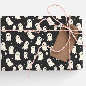 May include: Black gift wrap with a white ghost pattern. The gift is tied with pink and white twine and a brown gift tag.