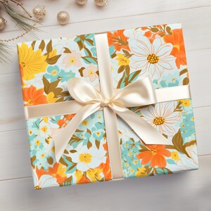 May include: A gift box wrapped in floral patterned paper with a light brown satin ribbon tied in a bow. The paper features a white background with orange, yellow, and blue flowers.