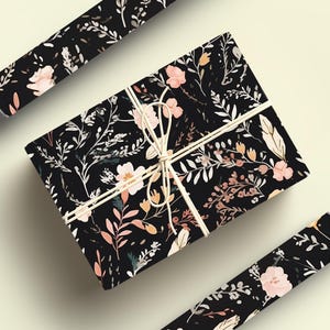 Op de afbeelding: Zwart cadeaupapier met een bloemenpatroon met roze en oranje bloemen en bladeren. Het cadeaupapier is vastgebonden met een wit touwtje.