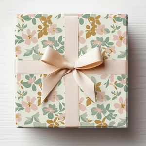 Op de afbeelding: Een cadeaudoos ingepakt in wit papier met een bloemenpatroon in roze, groene en gouden tinten. De doos is vastgebonden met een cr&egrave;mekleurig satijnen lint.